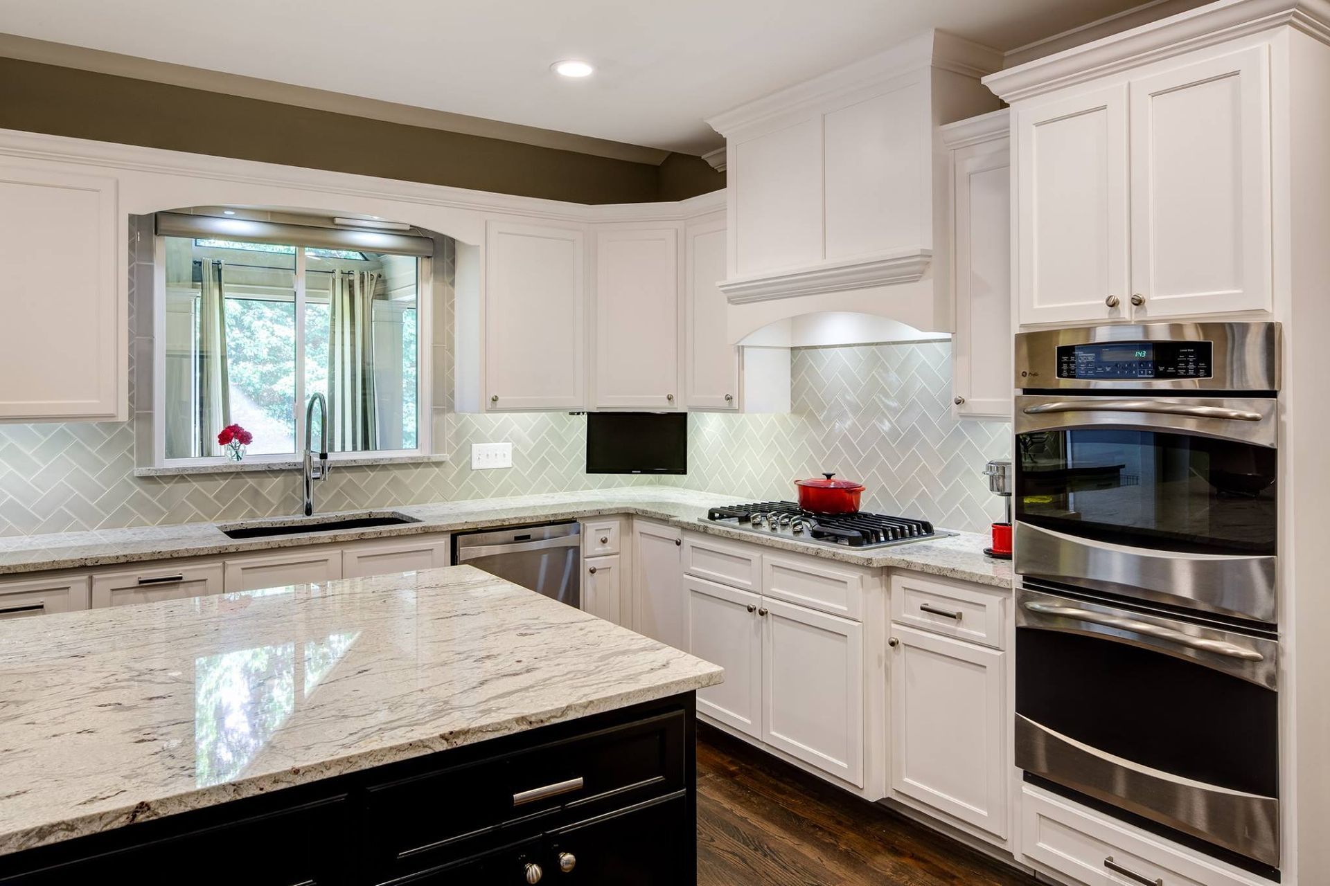 White kitchen with island, cabinets, stainless steel appliances, and window over a sink.