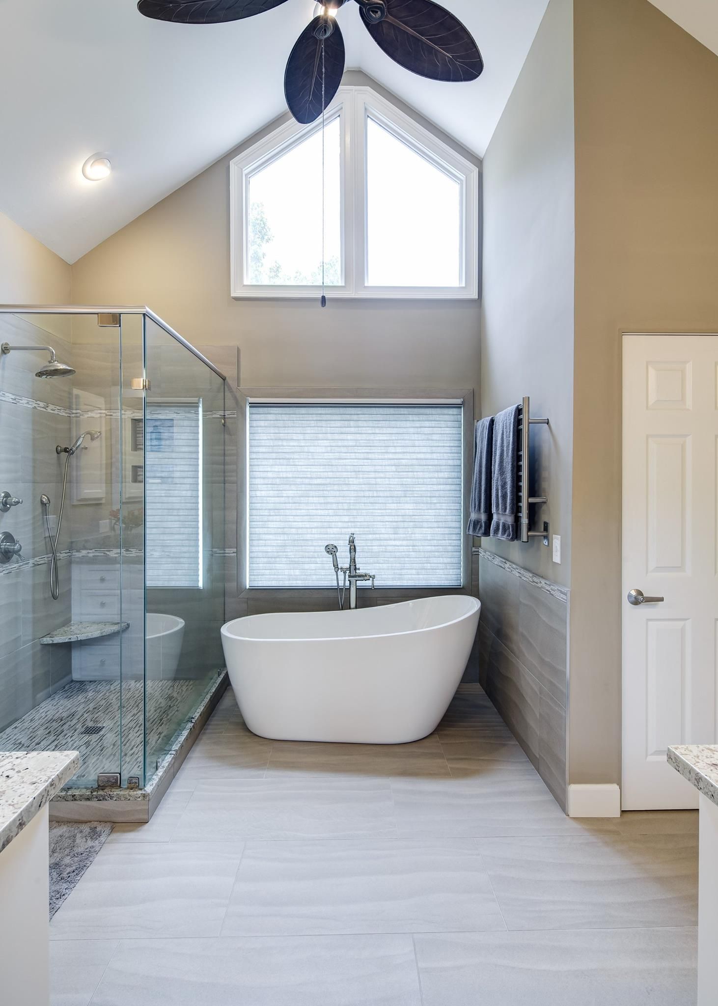 Bathroom with a freestanding white tub, glass shower, and light gray walls.