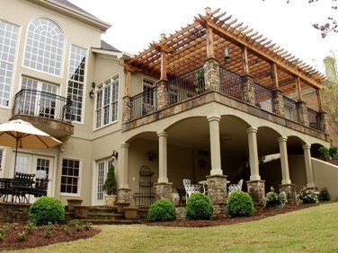 Beige home with a two-story deck featuring columns and a wooden pergola overlooking a grassy lawn.