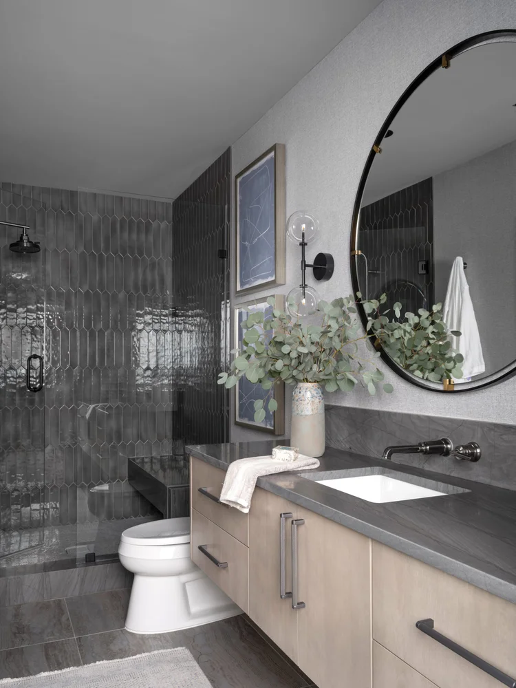 Modern gray bathroom with shower, vanity, and round mirror.