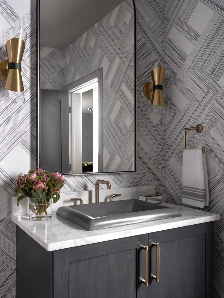 Powder room: gray vanity, marble countertop, geometric wallpaper, gold sconces, square sink, and mirror.