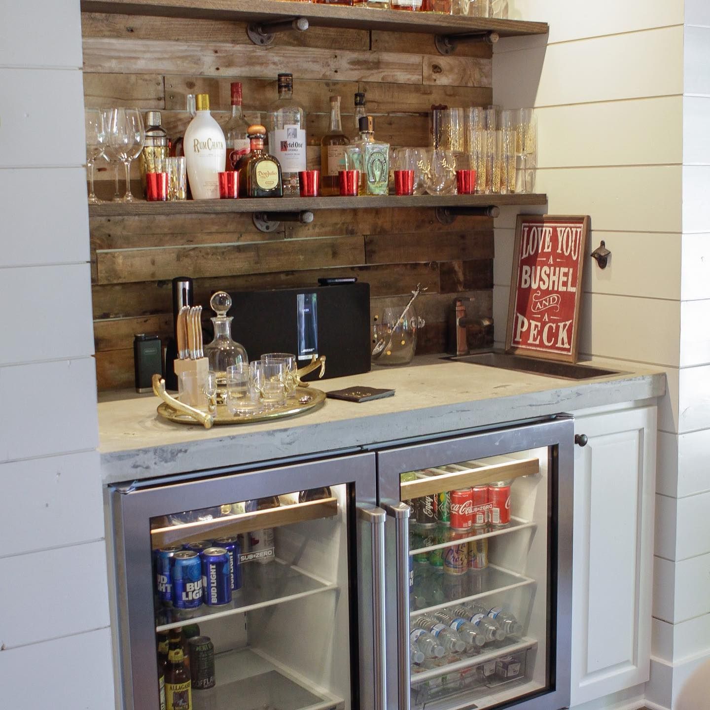 Built-in home bar with shelves, liquor bottles, glassware, and two mini-fridges stocked with drinks.