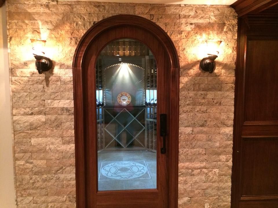 Arched wooden door to wine cellar with stone wall, sconces, and decorative glass.