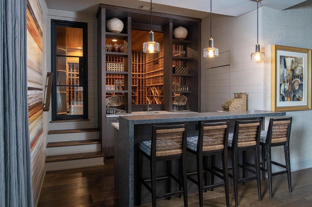 Wine bar with stone counter, dark wood shelves, stools, and a glass door to a wine cellar.