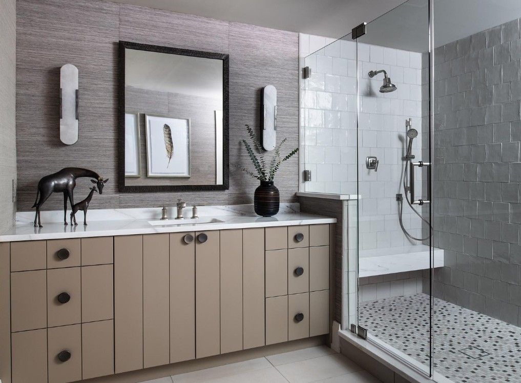 Modern bathroom with tan vanity, glass shower, gray walls, and decorative art.