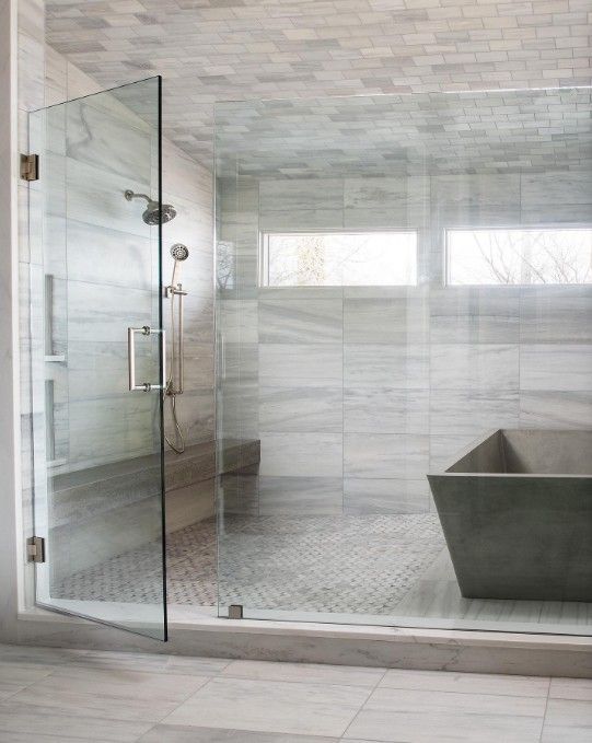 A modern, glass-walled shower with gray marble tile and a built-in bench.
