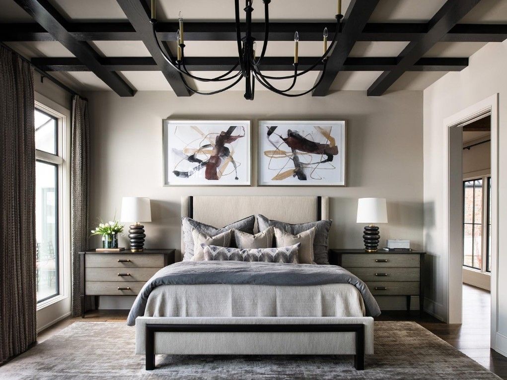 Elegant bedroom with a bed, nightstands, art, and dark wood ceiling beams; neutral tones.