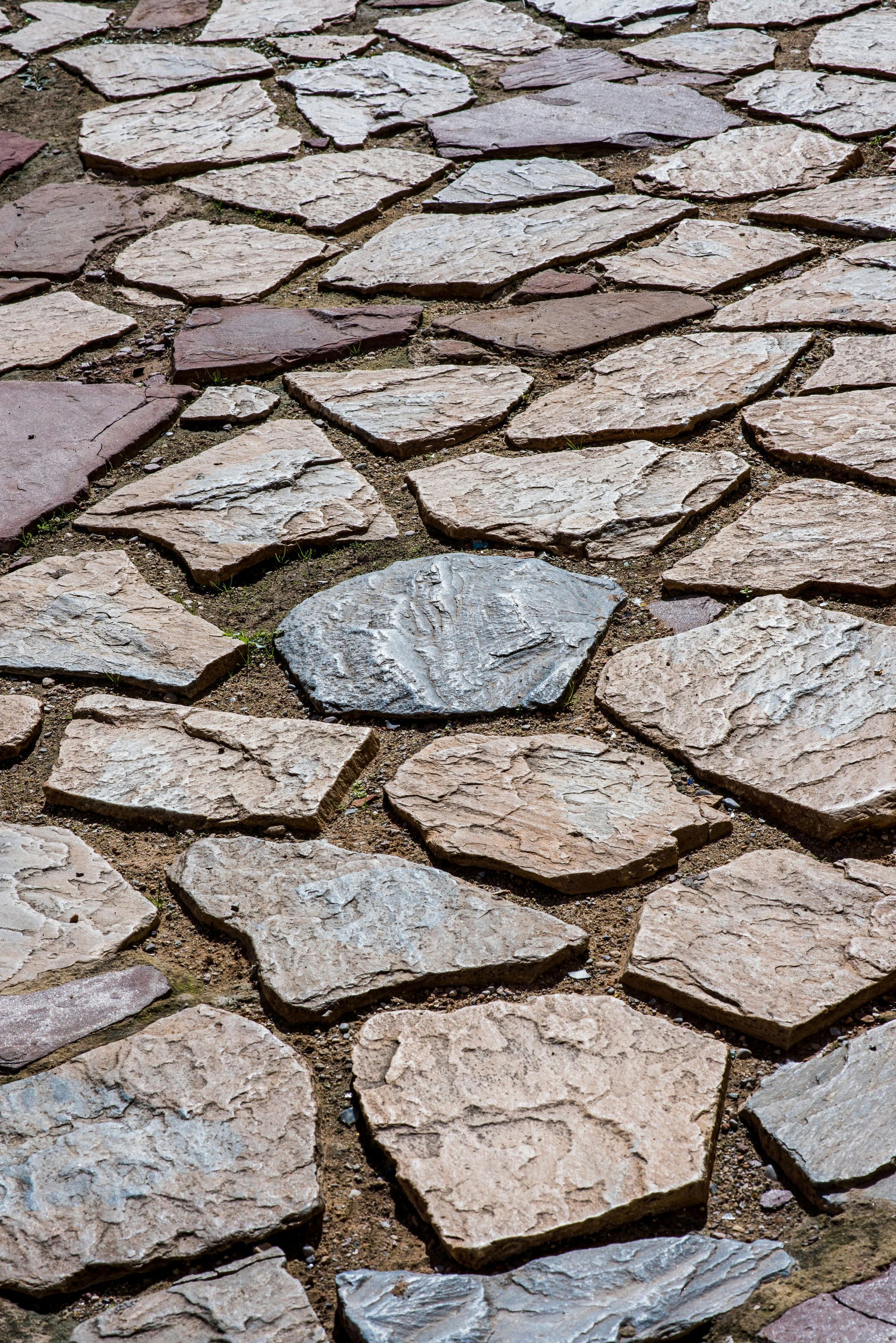 Stone pathway, made of irregularly shaped, earth-toned rocks, with visible sandy grout.