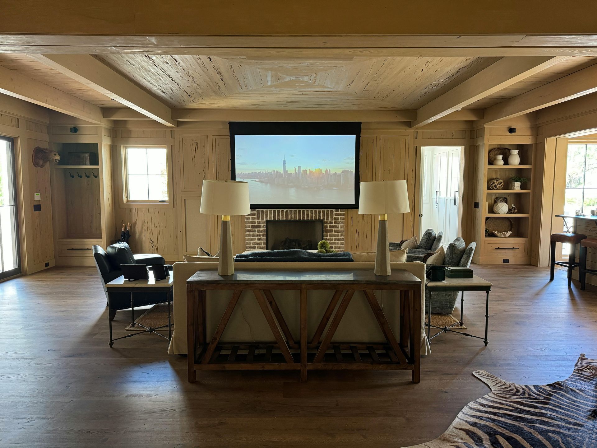 Living room with a mounted movie screen, two lamps on a console, and a zebra rug on a hardwood floor.