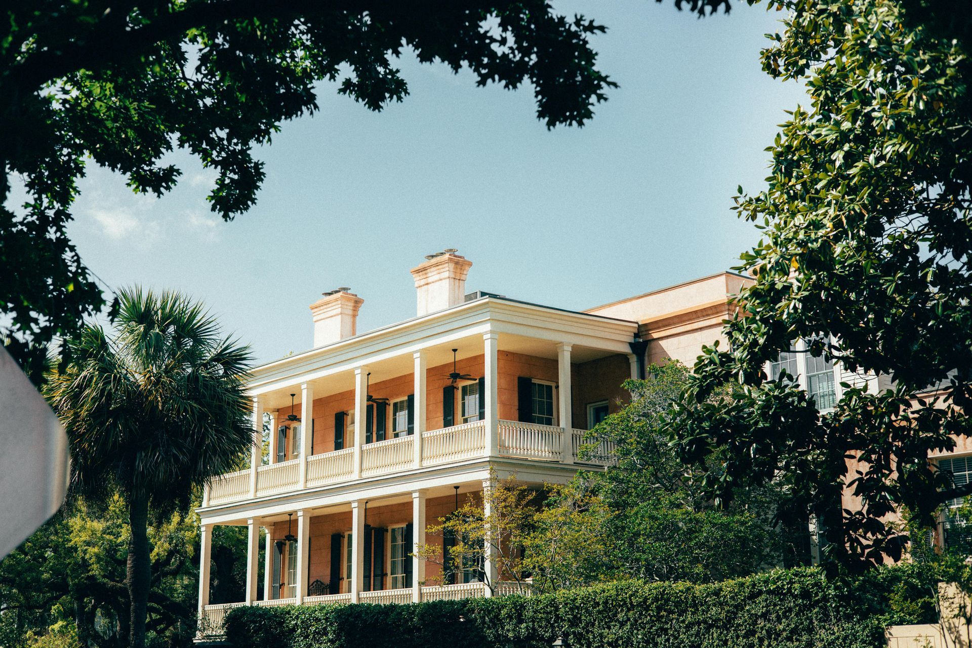 Two-story pink mansion with white balconies and columns, trees frame the view in Charleston, SC.