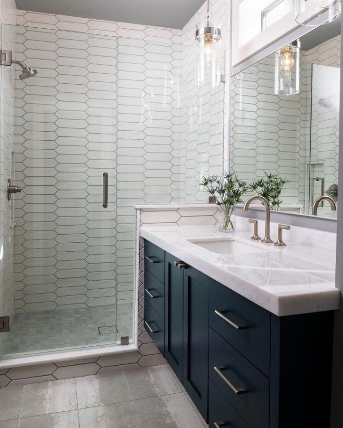 Bathroom with navy blue vanity, marble countertop, white elongated tile shower, and glass door.