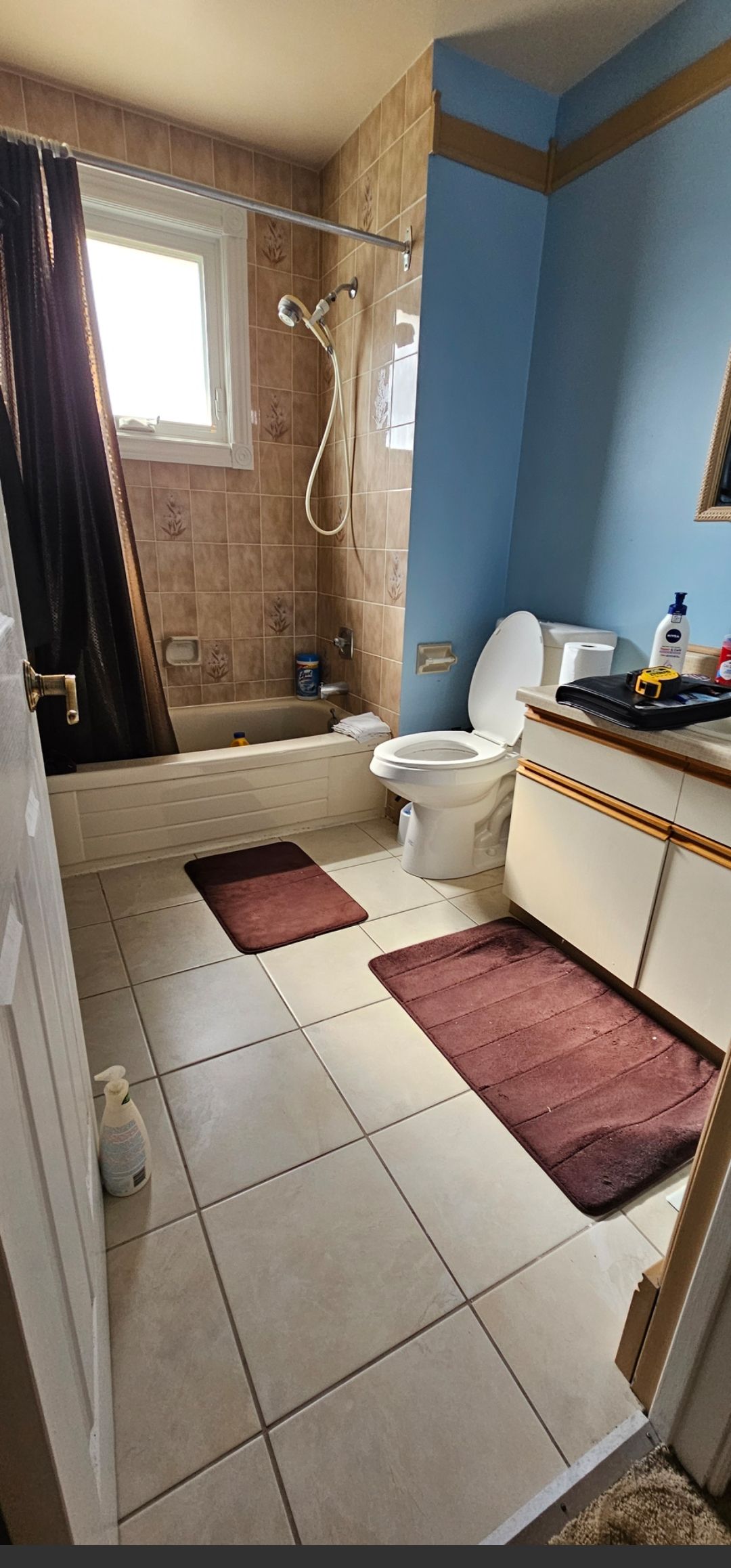Bathroom with brown tile, a blue wall, white toilet, and brown bathmats on the floor.