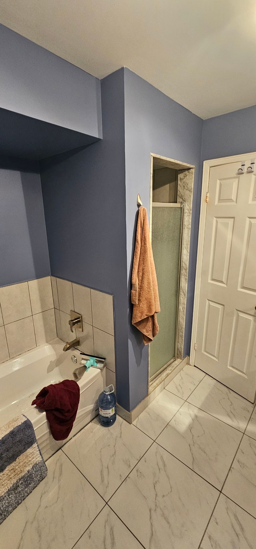 A blue-walled bathroom with a bathtub, shower, and a closed white door.