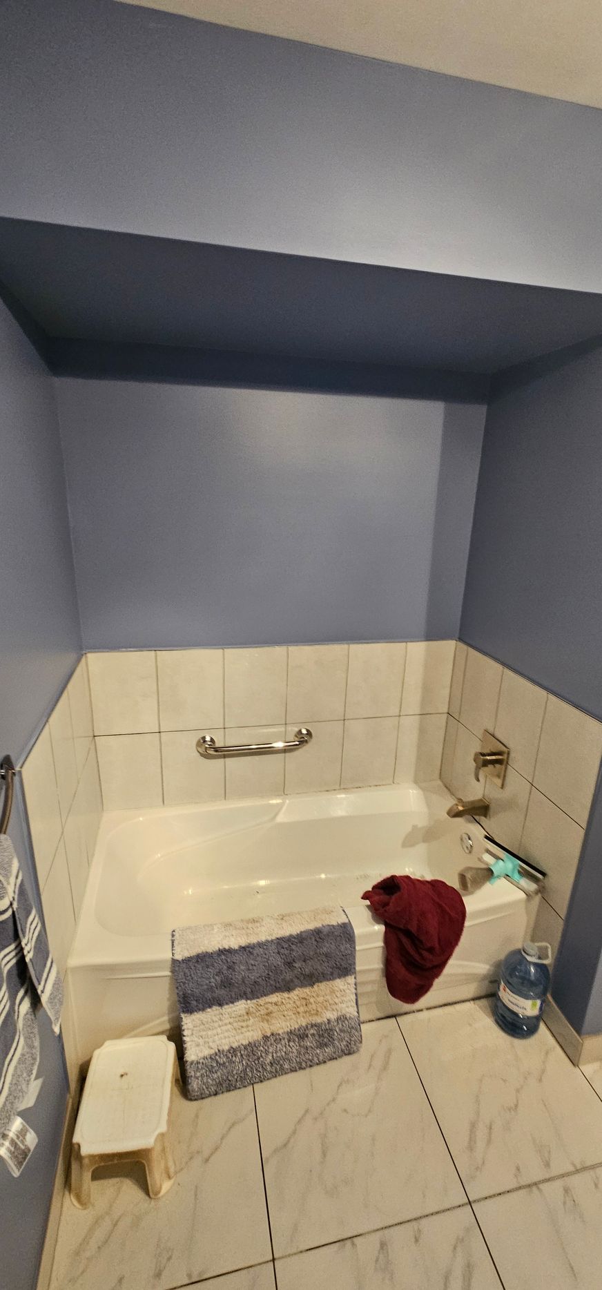 Bathroom with a blue ceiling and walls, a white tub, and tile floor. A red towel, a mat, and a stool are in view.