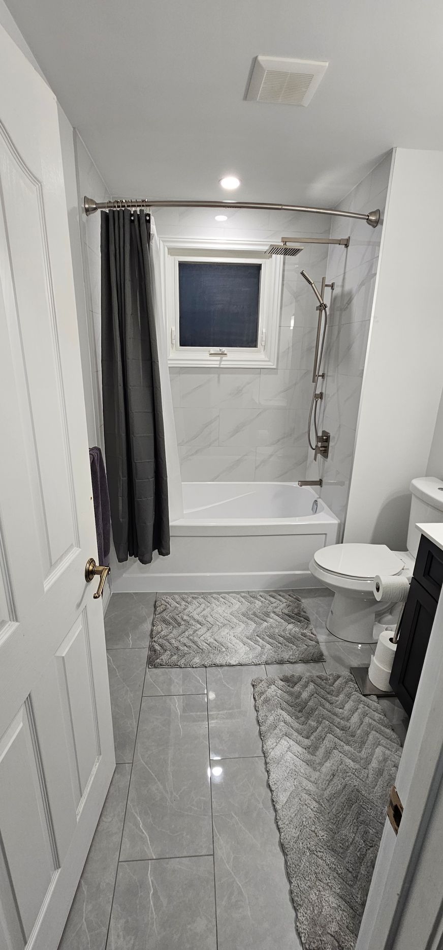 Bathroom with white tile, a bathtub, and two gray rugs.