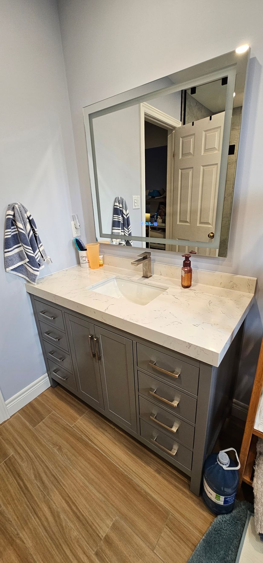 Bathroom vanity with a gray cabinet, marble countertop, and large mirror.