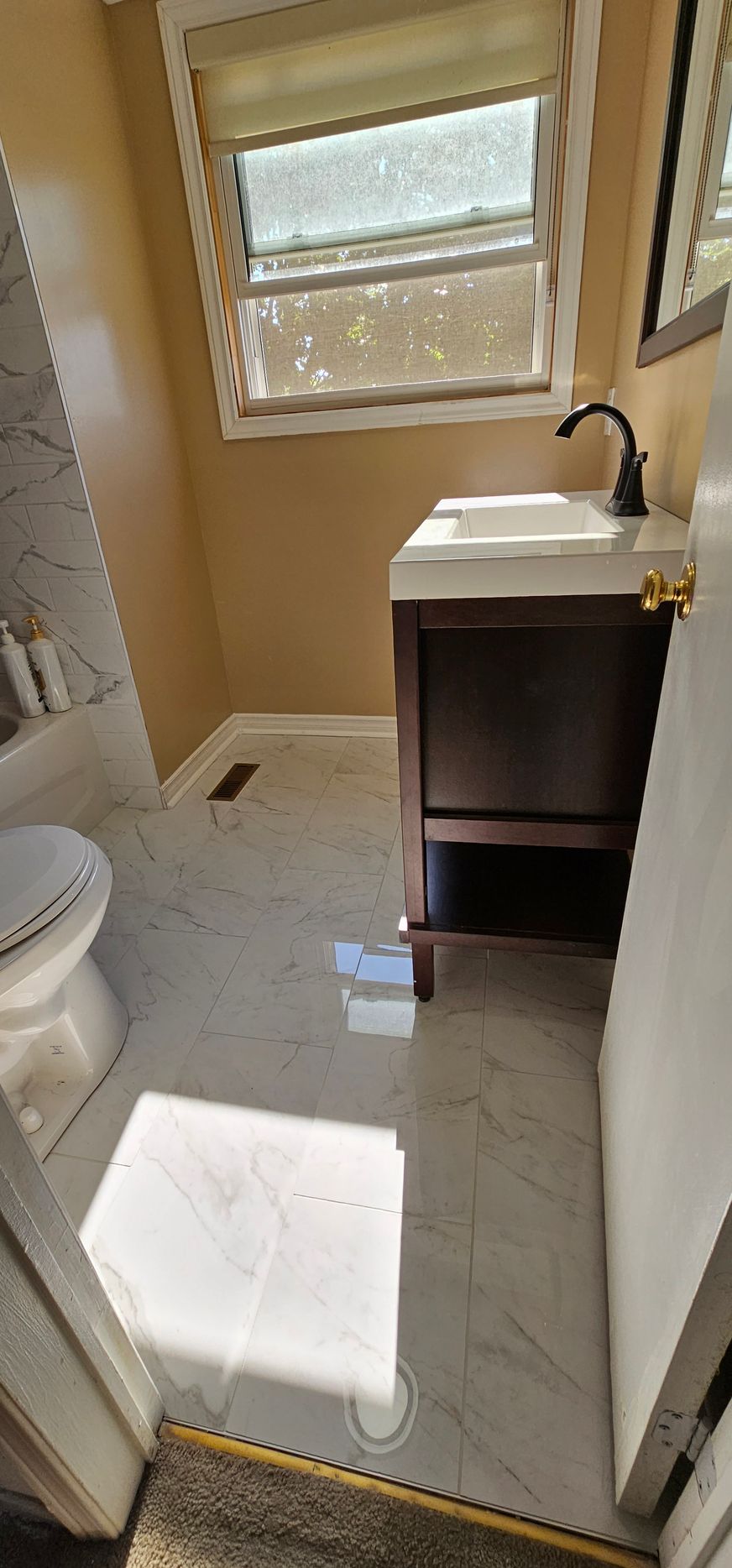 Bathroom with white marble floor, dark vanity, and window. Sunlight reflects off the floor.