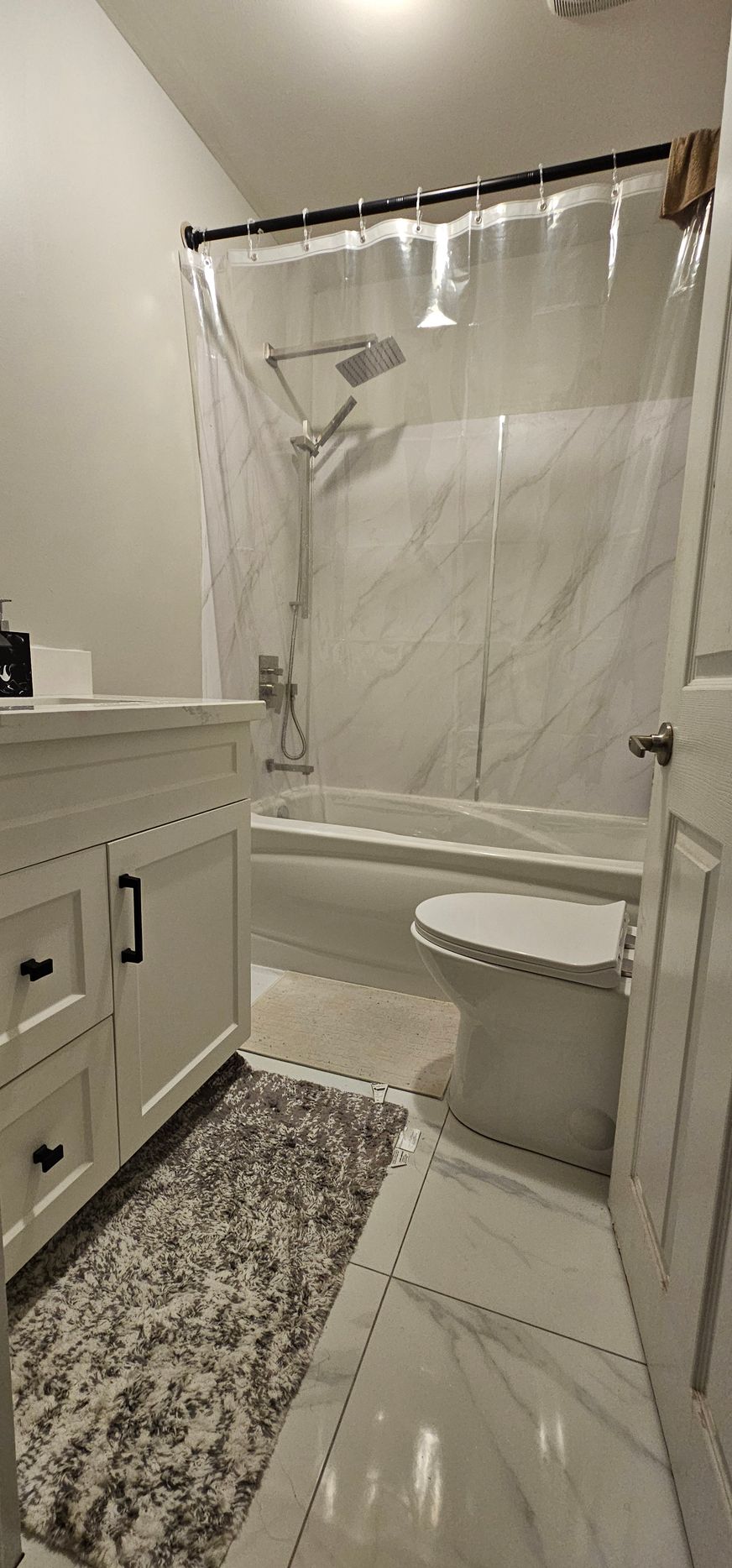 Bathroom with white vanity, toilet, and marble tile. Clear shower curtain.