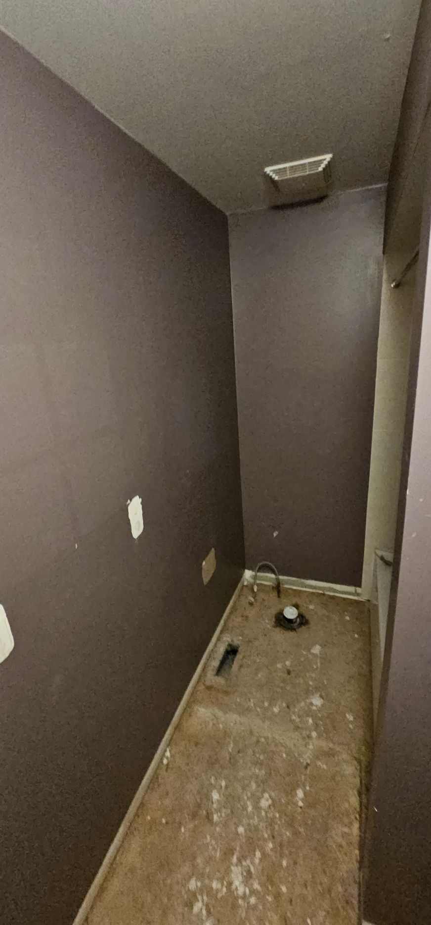 An empty room with dark purple walls and a damaged floor. A ceiling vent is visible.