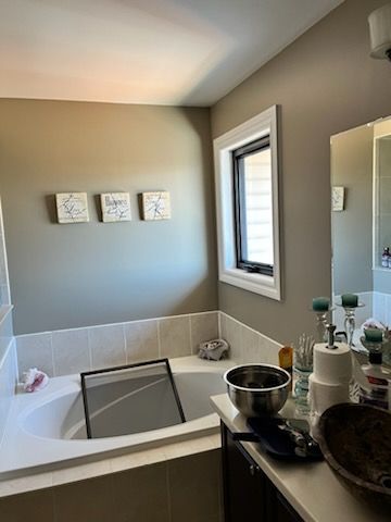 Bathroom with a white tub, window, and vanity. Gray walls, artwork, and a screen inside the tub.