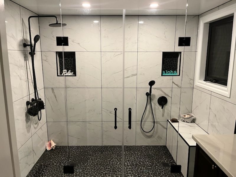 Modern bathroom with marble tile, black fixtures, pebble floor, and glass shower doors.