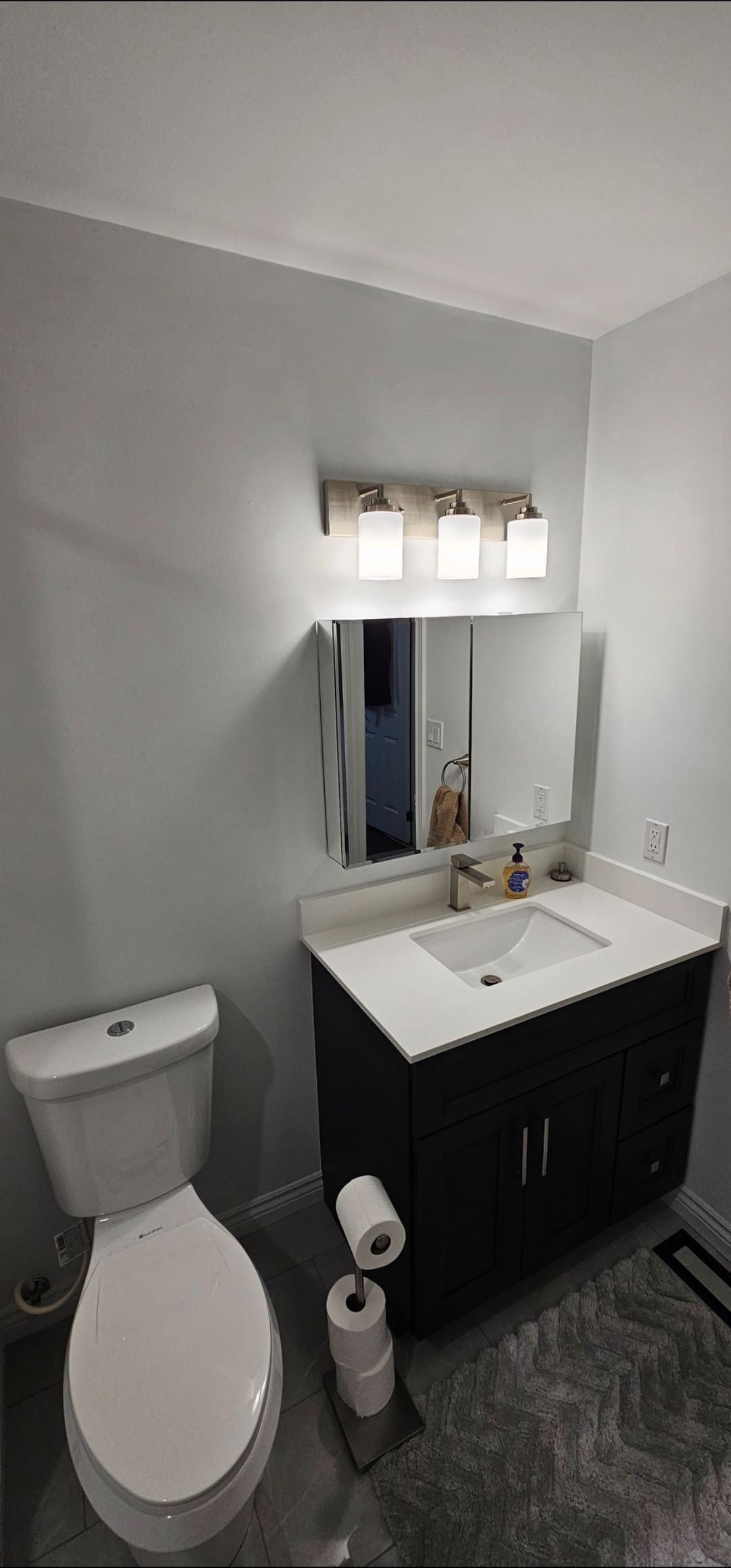 A bathroom with a toilet, vanity, and mirror. White and gray tones are dominant.