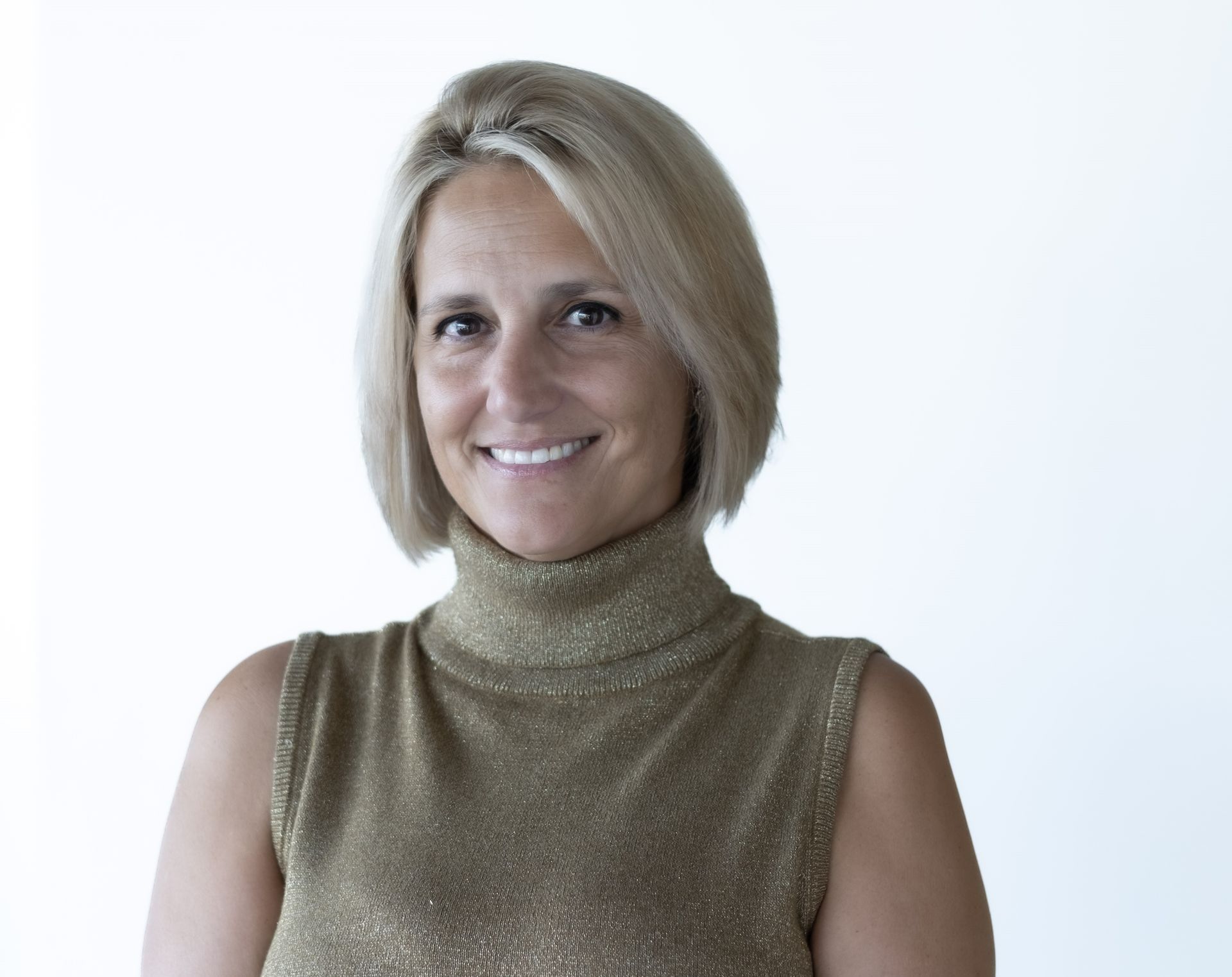 Woman with blonde bob haircut wearing a gold turtleneck, smiling.