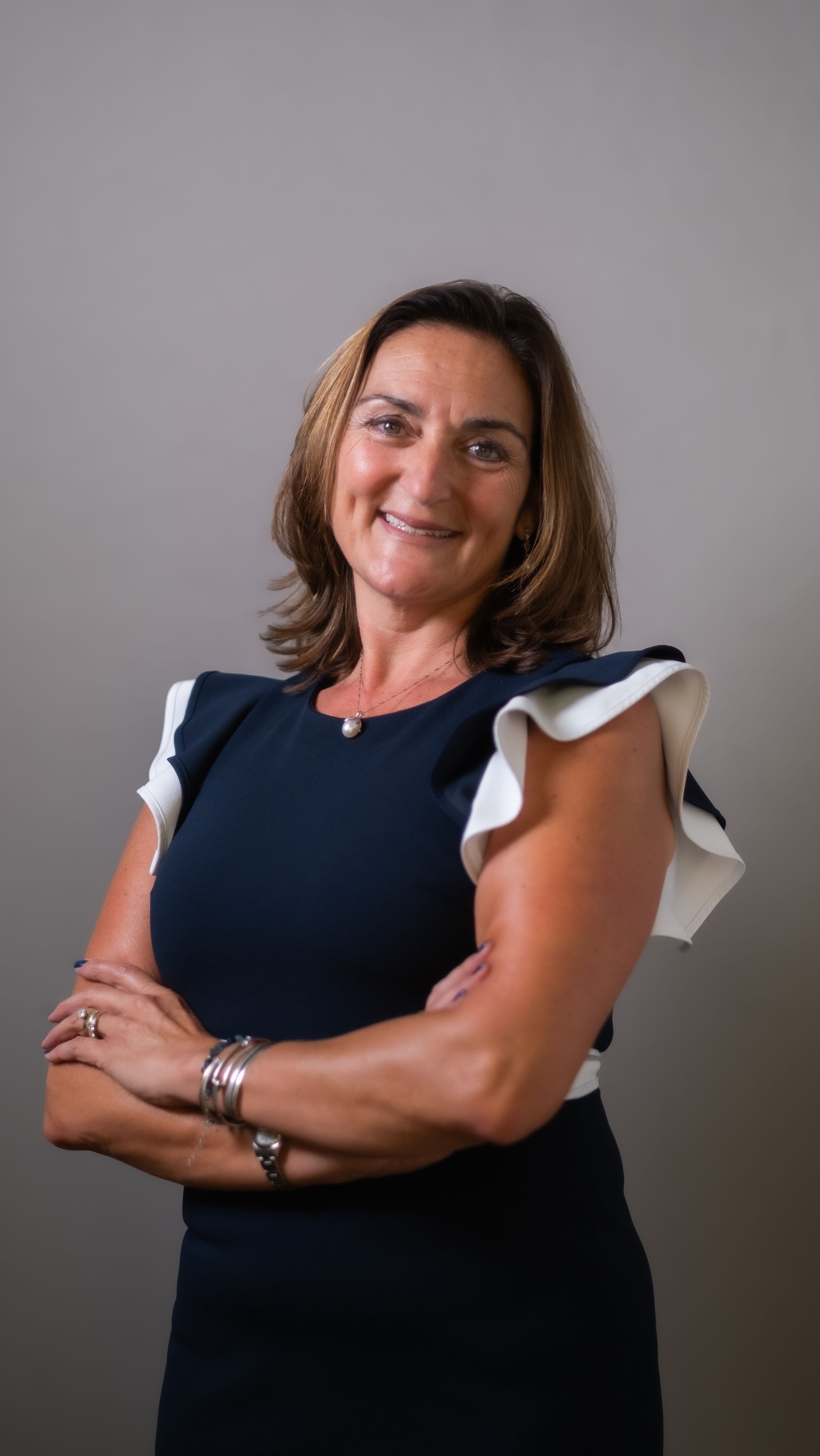 Woman with brown hair, smiling, wearing a black top and silver necklace, outdoors.