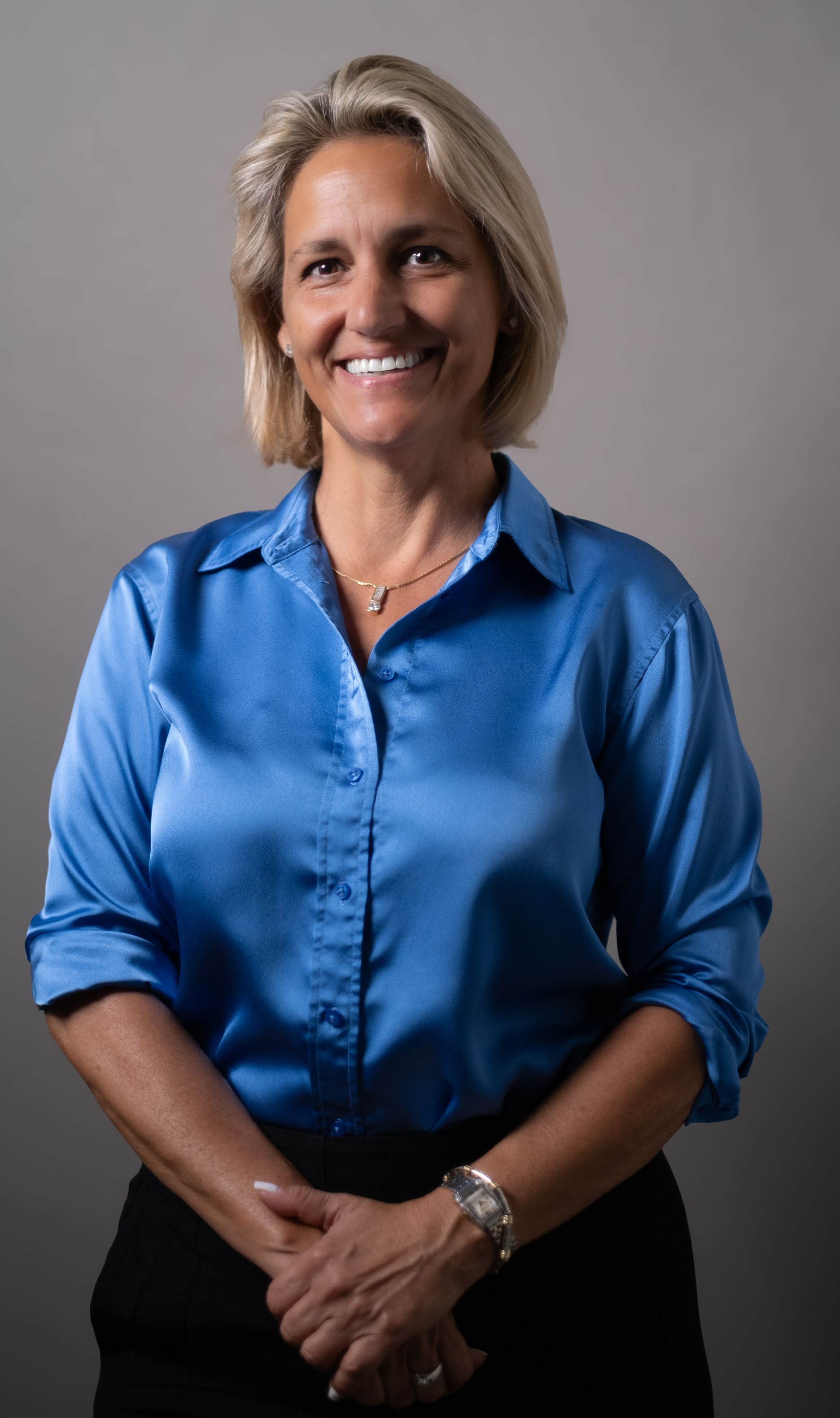 Woman with blonde bob haircut wearing a gold turtleneck, smiling.