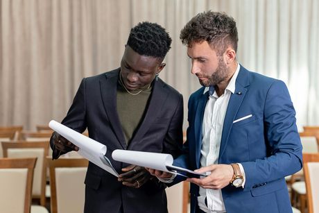 Two men in suits are looking at a piece of paper.