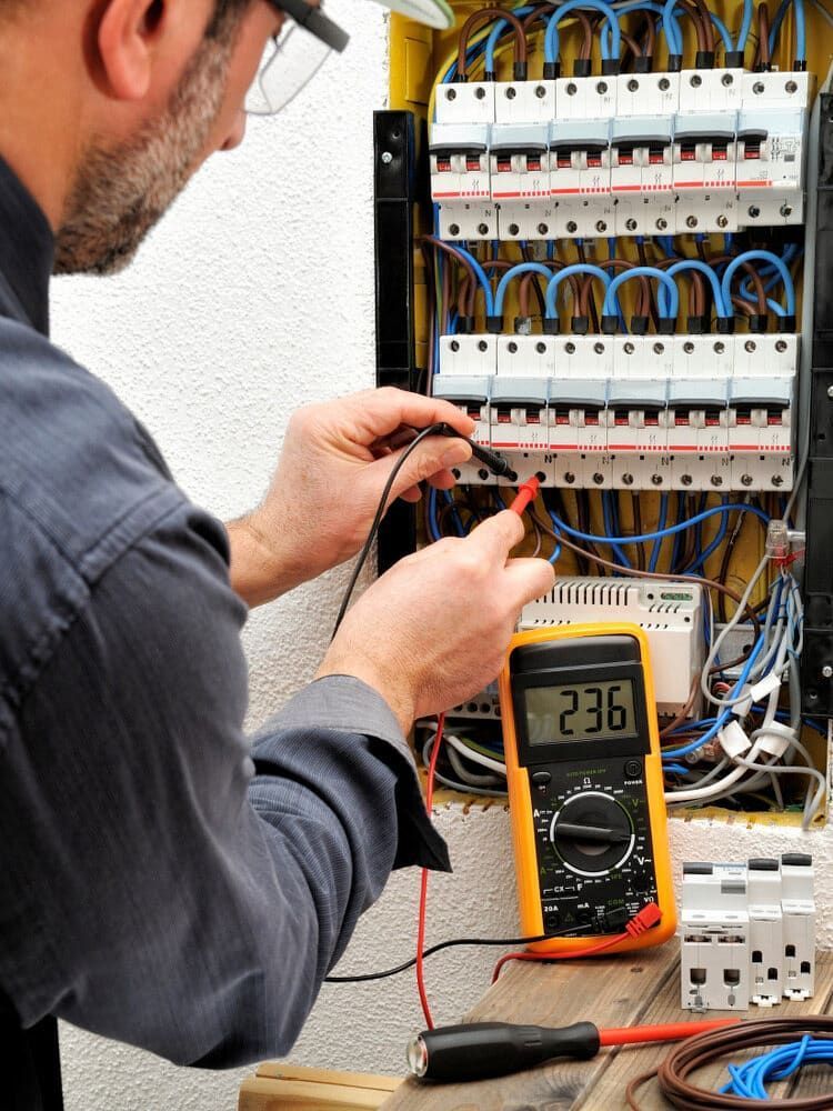 Electrician using a yellow multimeter to test voltage on a circuit breaker panel. — Brett Cox Electrical and Solar in Gumly Gumly, NSW