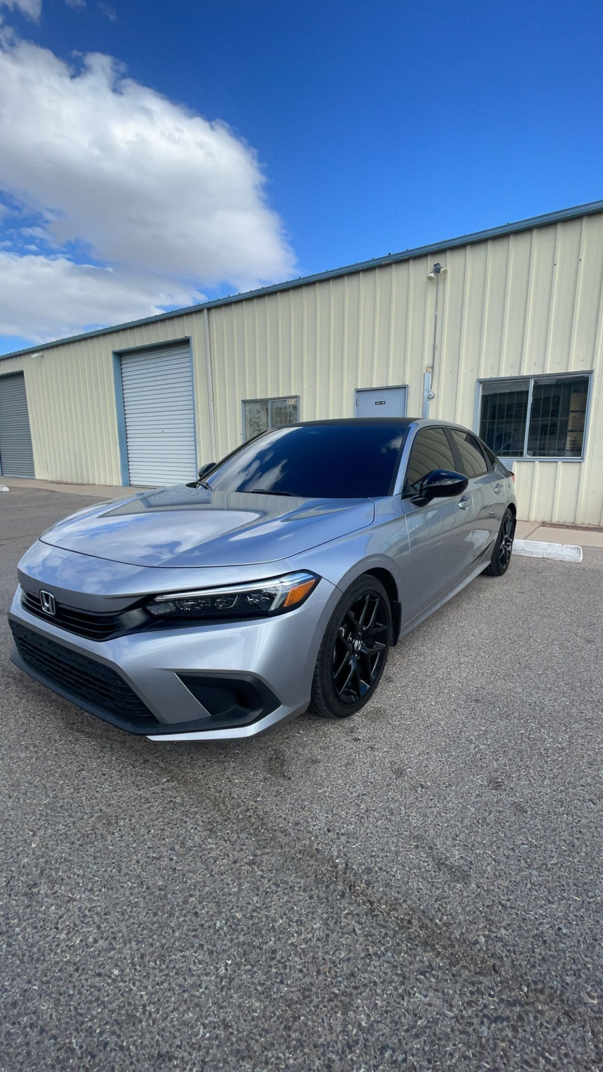 A silver honda civic is parked in front of a building.