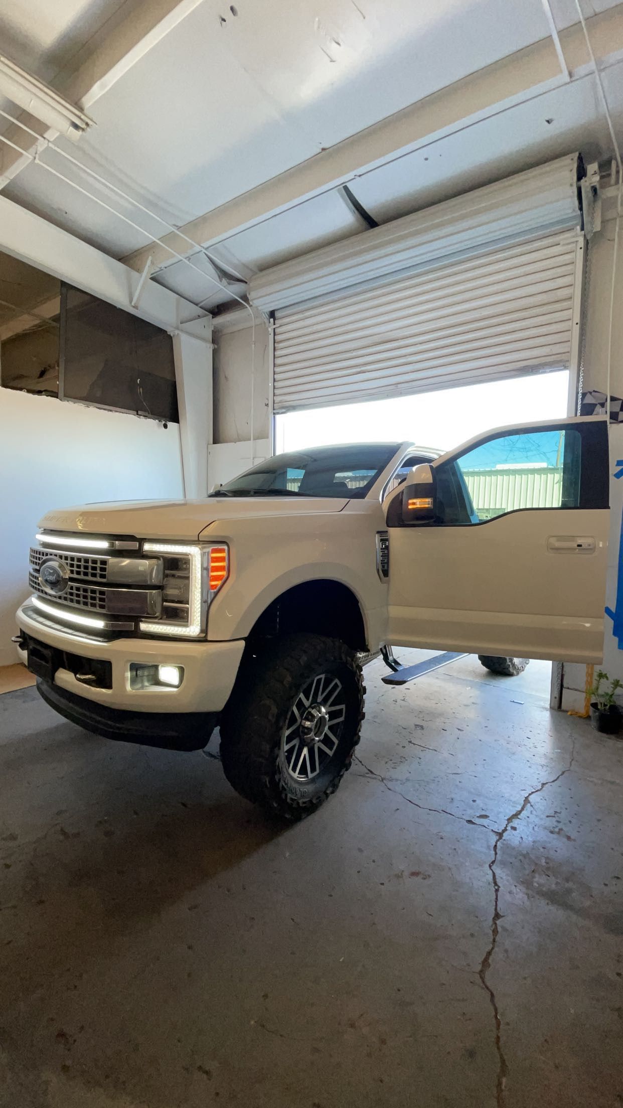 A white truck is parked in a garage with its doors open.