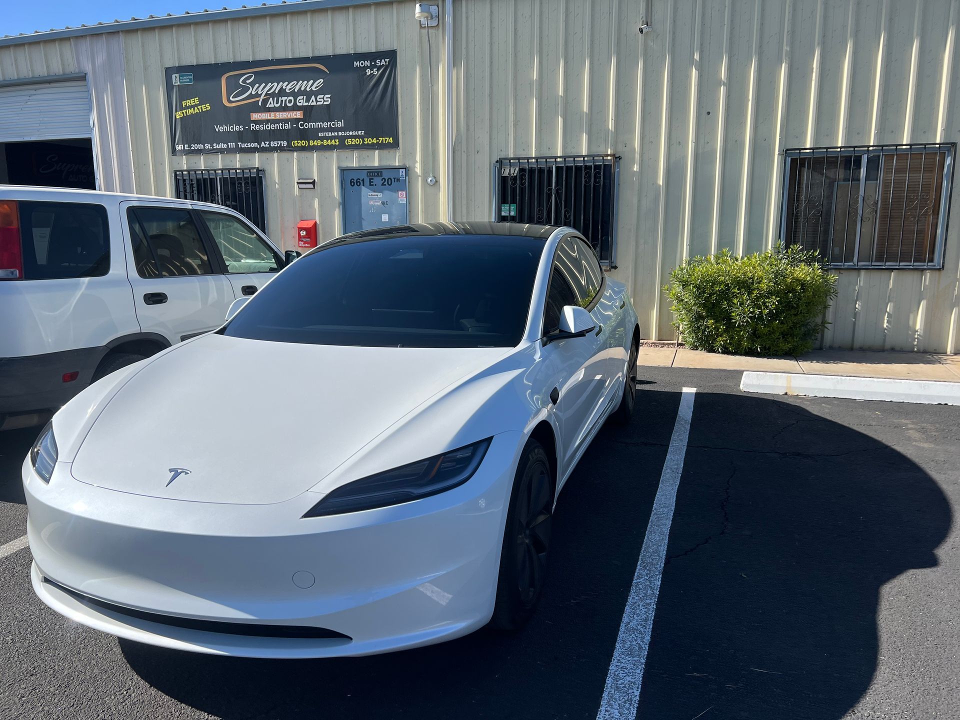 A white tesla model 3 is parked in front of a building.