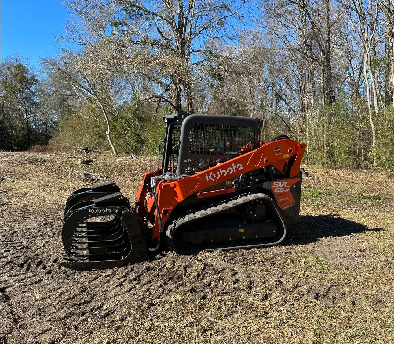 A bulldozer with a grapple attached to it is sitting in a dirt field.