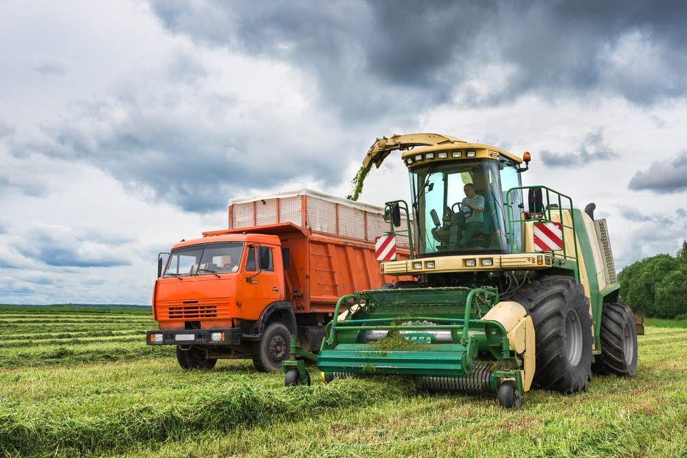 A Tractor Is Cutting Grass In A Field Next To A Dump Truck — Dillon Rural In Cundletown, NSW