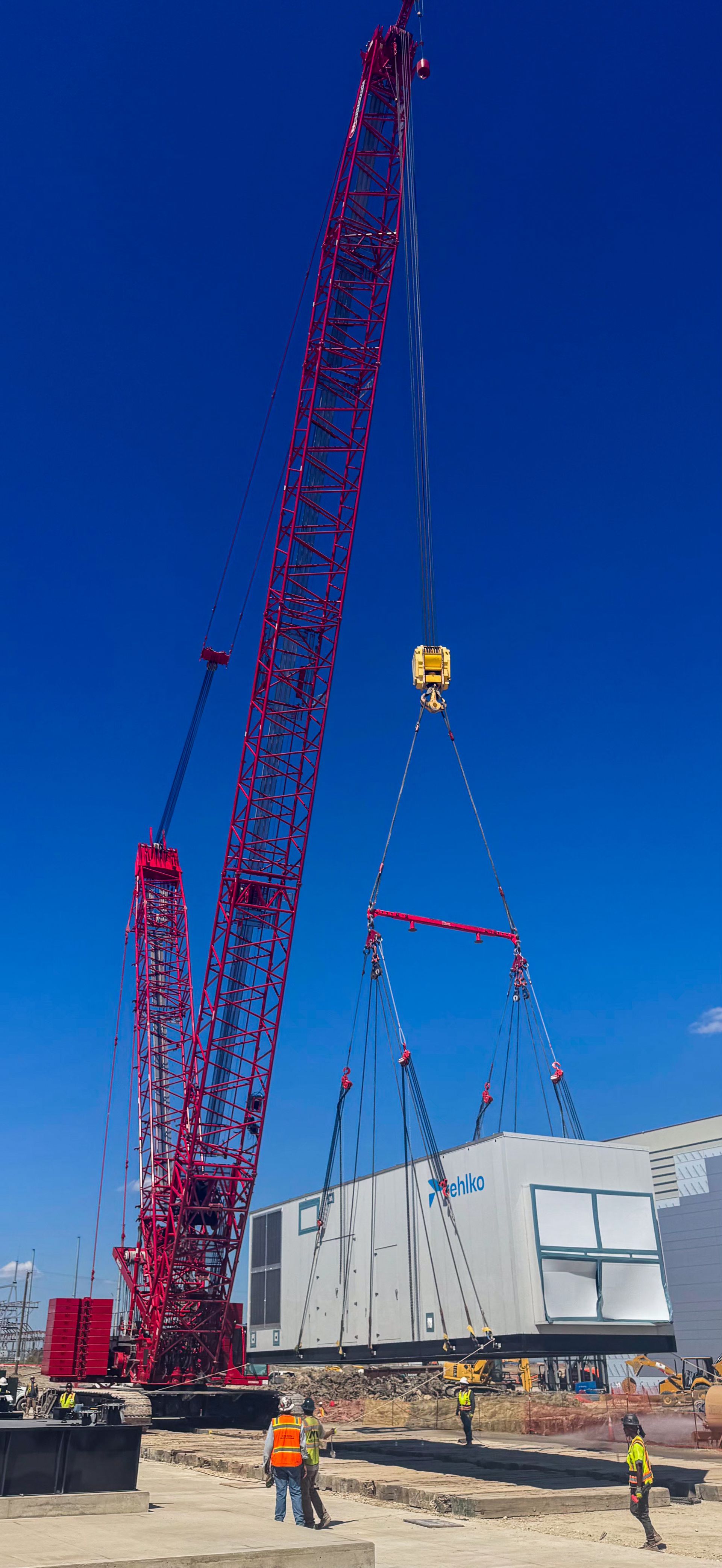 A large red crane lifts a component above a building under construction on a sunny day.