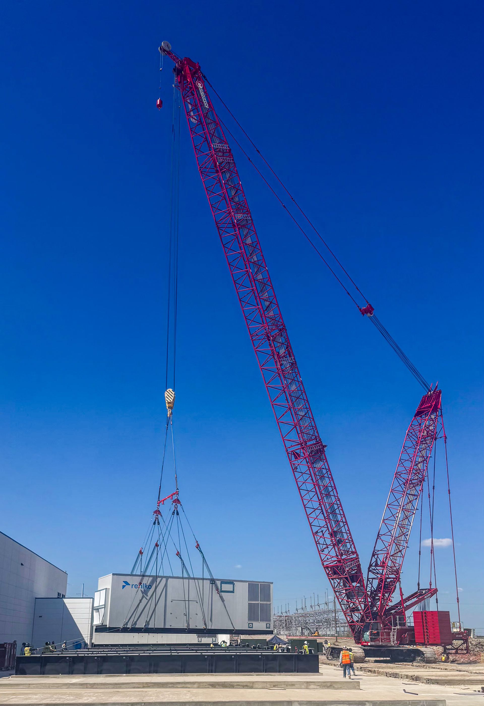 A large red crane lifts a rectangular container on a construction site under a blue sky.