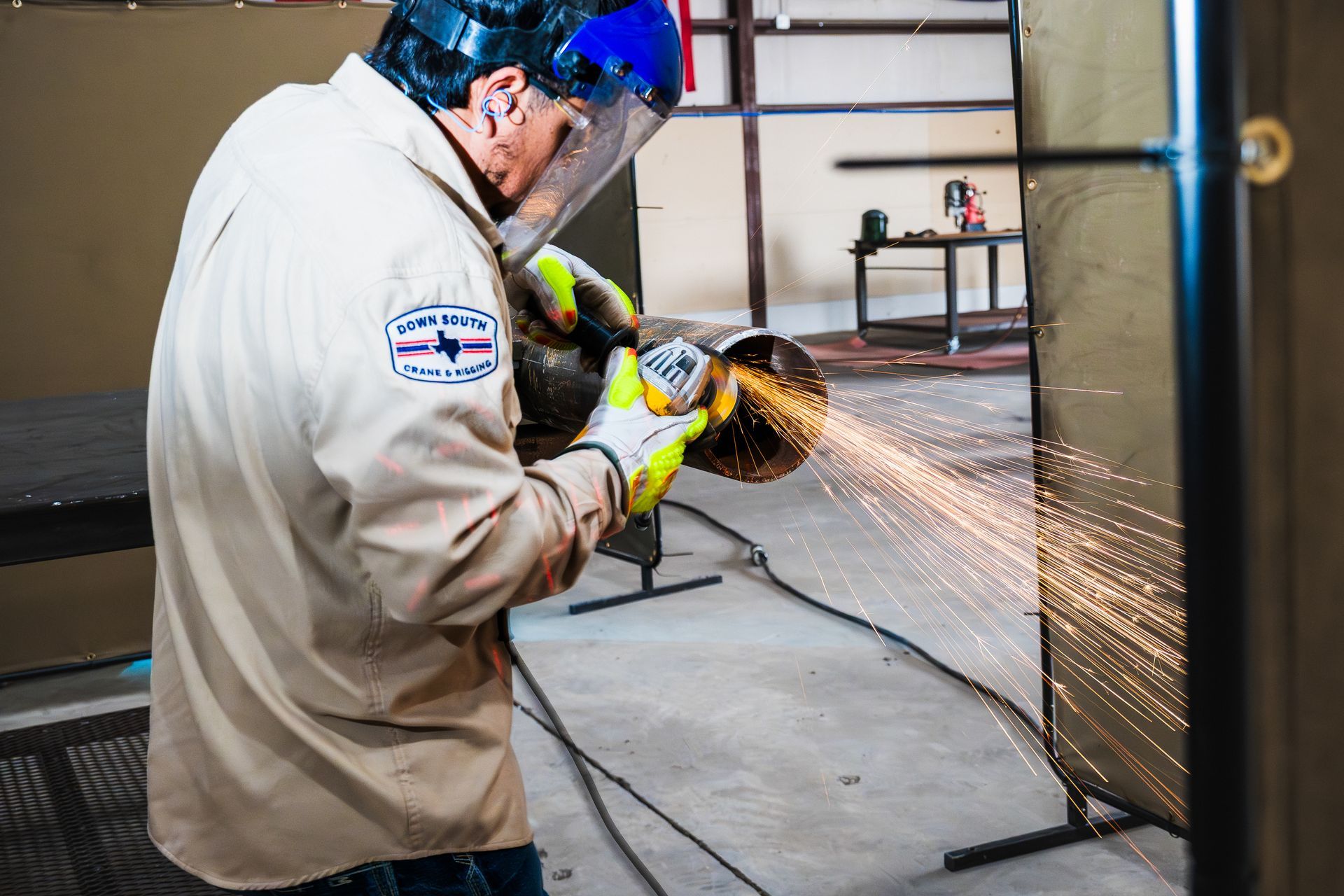 A worker in protective gear using an angle grinder on a metal pipe, creating sparks.