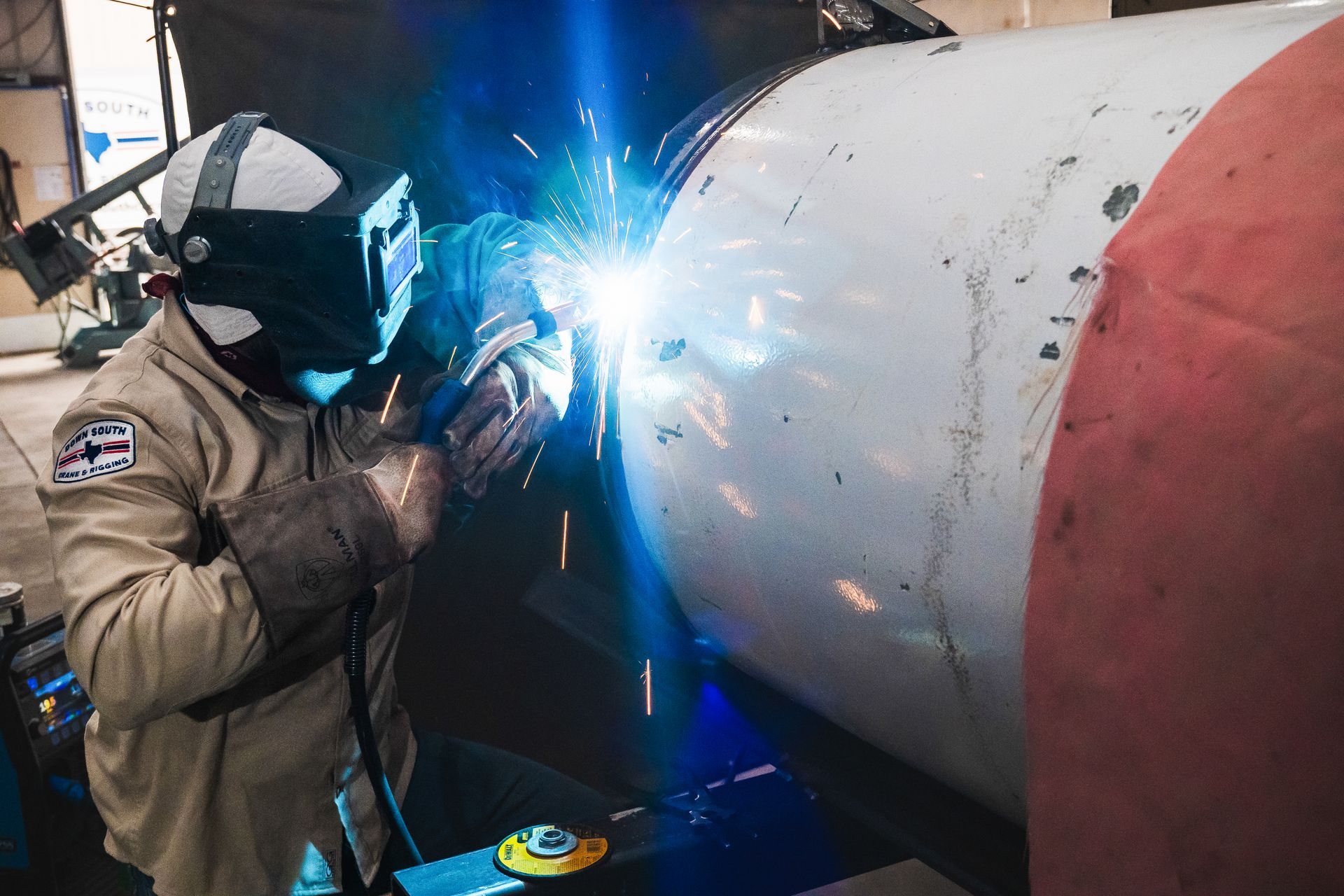Welder wearing protective gear welding a large, cylindrical metal object, with bright sparks.