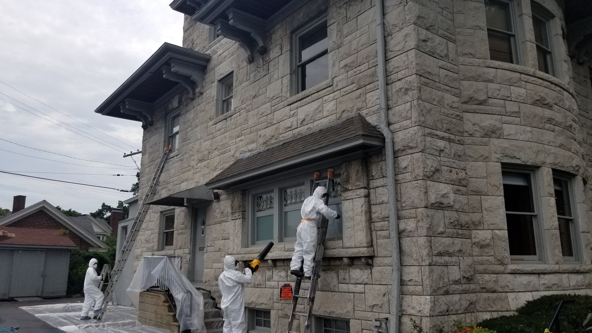 3 people in hazmat suits removing lead paint from old stone house