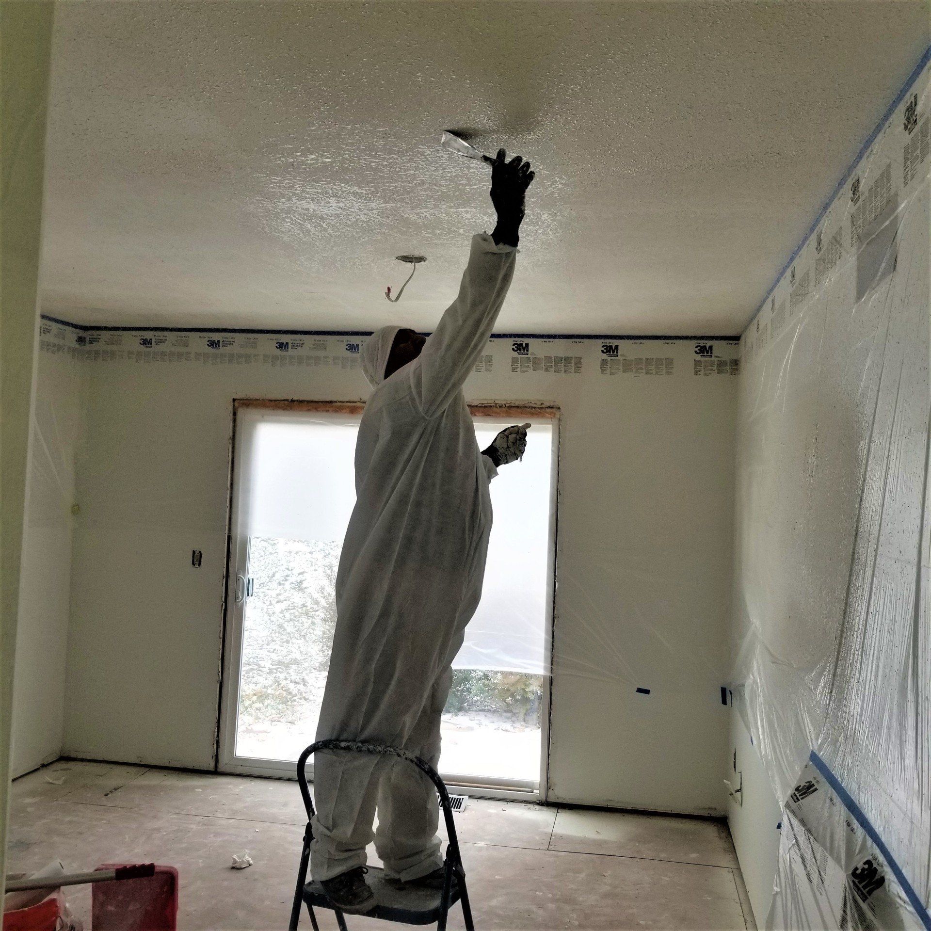 Painter on a step ladder smoothing a knockdown texture finish on the ceiling of a bedroom
