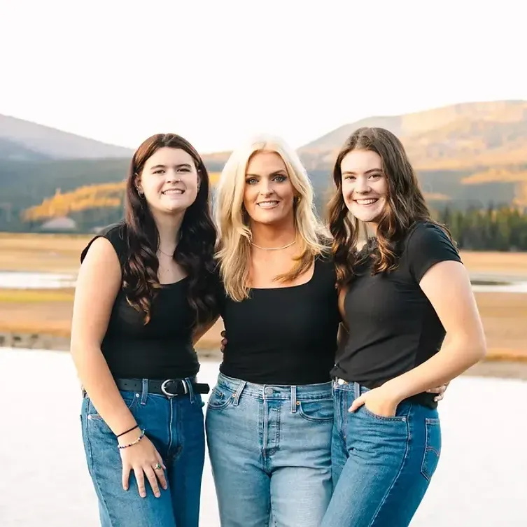 Three women are posing for a picture in front of a body of water.