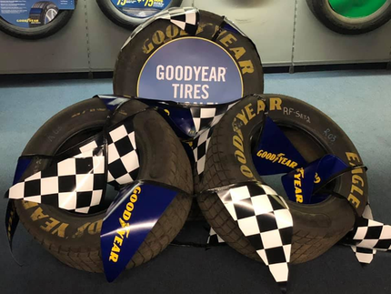 Goodyear Racing tire display with blue, black, and checkered tires arranged on a wall shelf | Dean's Tire & Auto