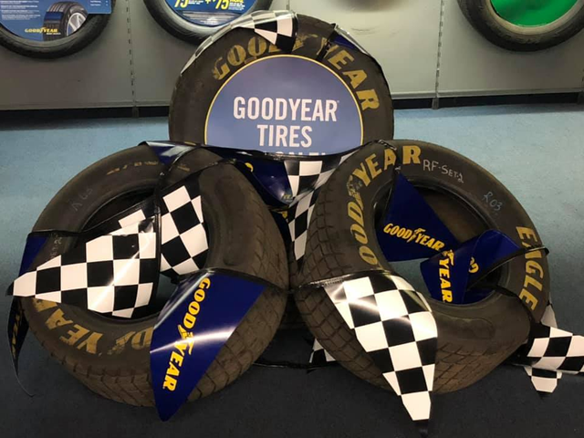 Goodyear Racing tire display with blue, black, and checkered tires arranged on a wall shelf | Dean's Tire & Auto