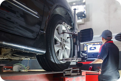 Car being inspected on an alignment lift while a mechanic works at a computer in an auto shop | Dean's Tire & Auto