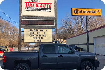 Dark pickup truck parked in front of a tire shop with Firestone and Continental signs. | Dean's Tire & Auto