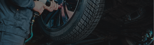 Close-up of a car wheel and a person crouching beside it in a dark setting | Dean's Tire & Auto
