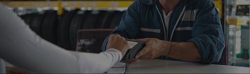 Person signing paperwork across a table from another person in an office setting | Dean's Tire & Auto