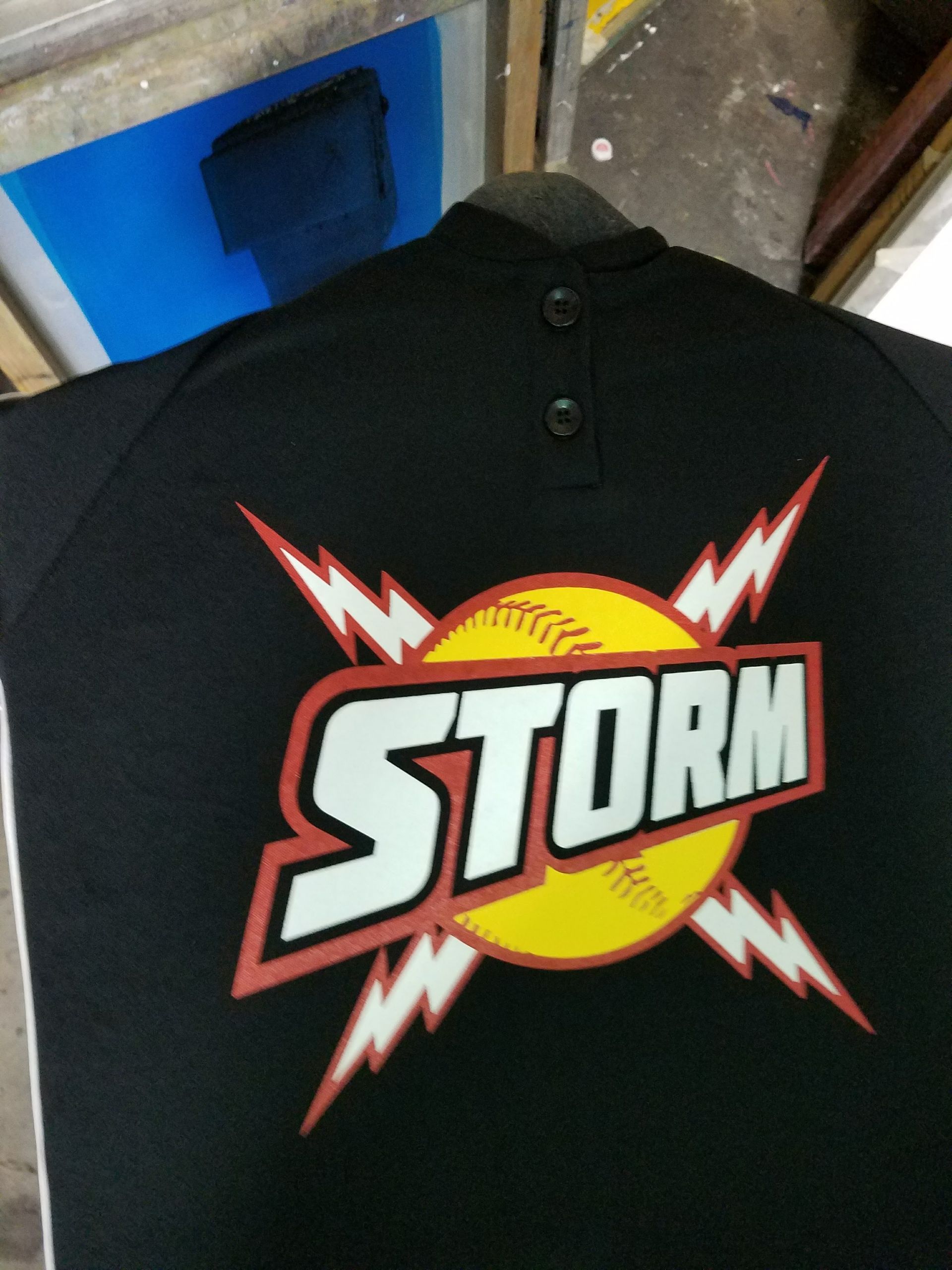A black shirt with a graphic featuring a yellow softball, white lightning bolts, and the text 